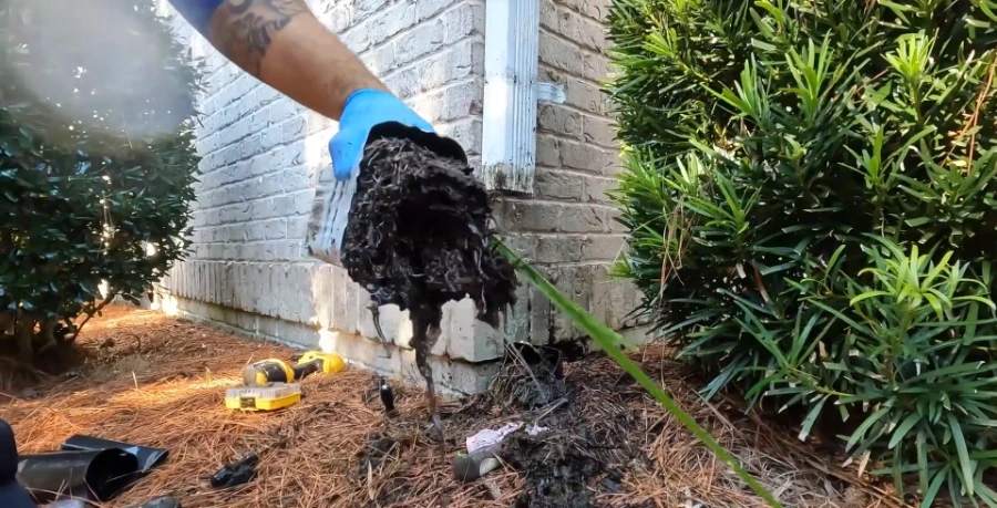 Debris removal from a clogged downspout in Greenville SC, compacted leaves and sweetgum pods extracted from elbow section
